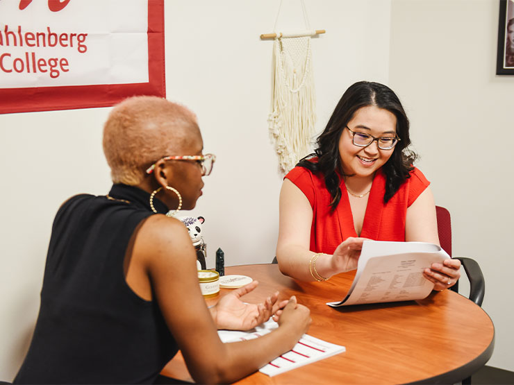 A career counselor speaks with a college student at a table in an office.