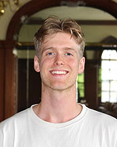 Individual standing smiling wearing white tee-shirt.