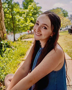 Counseling trainee smiling wearing blue tank top in front of landscape painting.