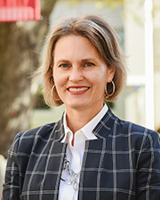 Woman wearing plaid jacket with lighter collared shirt standing posed outdoors on Muhlenberg College campus.