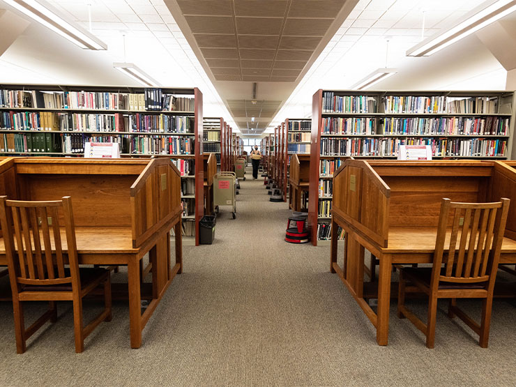 Wooden desks and bookshelves stand symmetrically in a library.