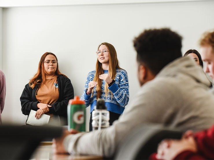 A pair of students speak to a class while others look on.