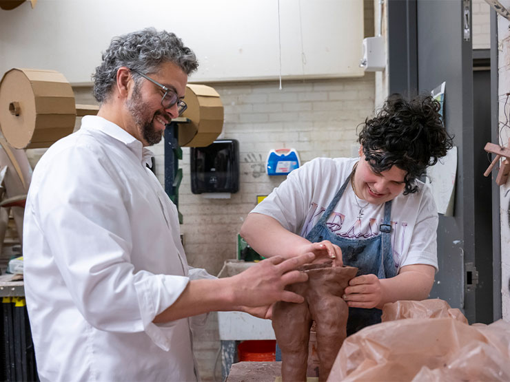 An instructor assists a student create a clay sculpture in a workshop.