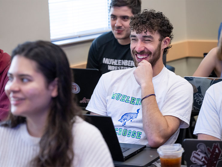 A classroom of young adults look toward the front of the room, many of the faces grinning.