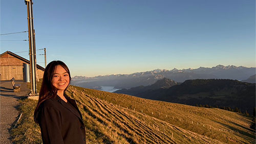 A college student in front of a field and mountains in Switzerland