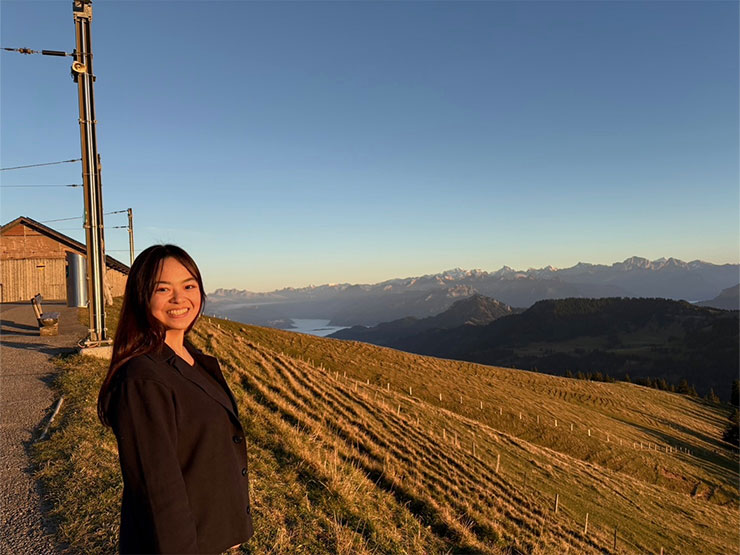 A college student in front of a field and mountains in Switzerland