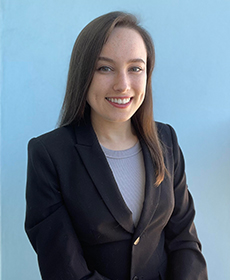 A person wearing a black blazer and lilac-colored blouse, smiles at the camera.