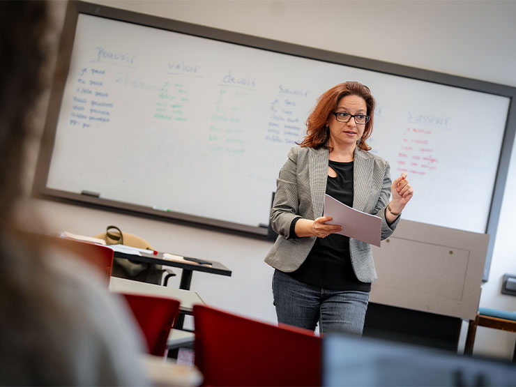 An instructor speaks in front of a classroom with French words written on a whiteboard.