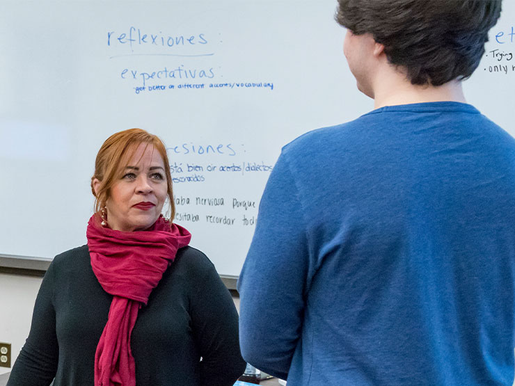 An instructor stands and looks at a student during a conversation in a classroom.