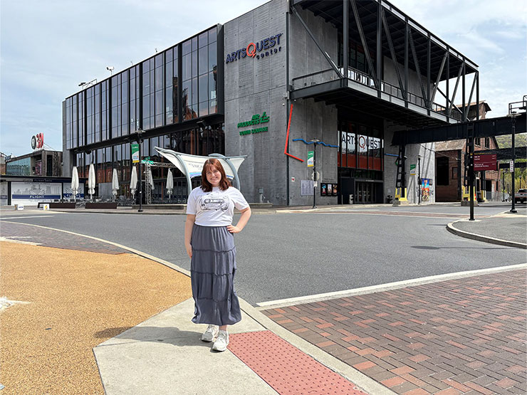 College student Marie Tohill stands, hands on hip, outside of the ArtsQuest building.