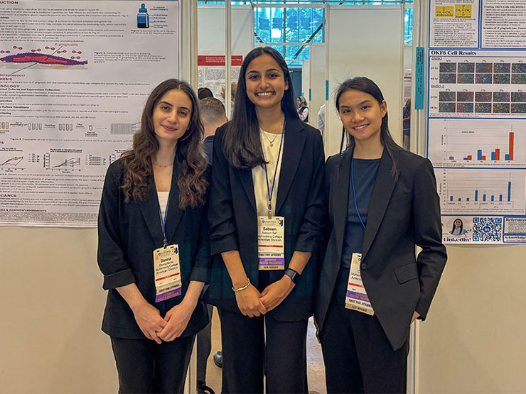 Three college students dressed professionally pose together in front of a poster display at a research conference.