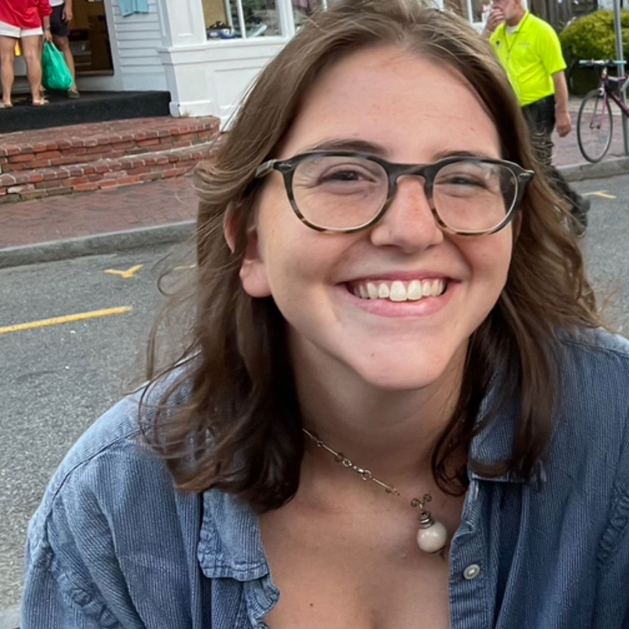 A woman with glasses smiles while outdoors.