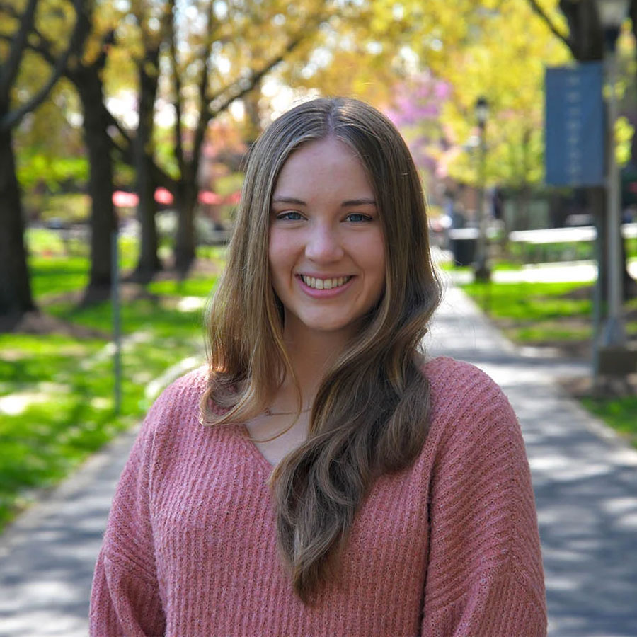 College student Sara Legnola smiles at the camera while standing outdoors on the campus of Muhlenberg College.
