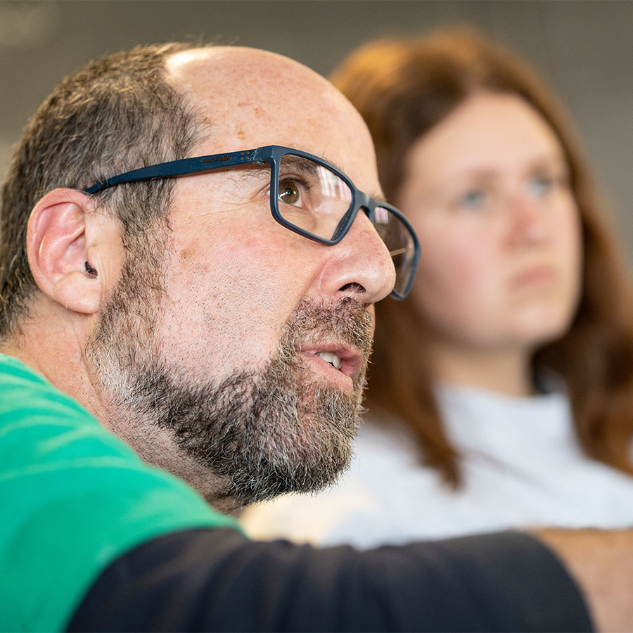 A closeup image of a college professor with glasses speaking to the class and looking off camera.