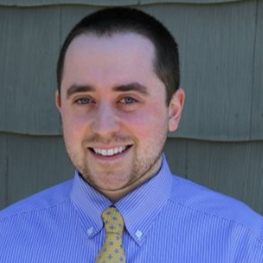 Bryan McCombs smiles in a dress shirt and tie.