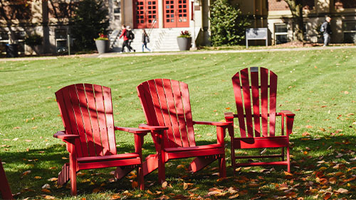 Three red Adirondack chairs sit on the lawn of the Muhlenberg College campus.