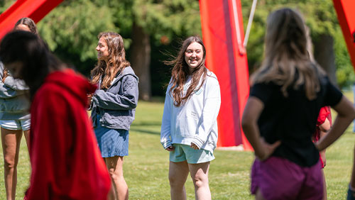 A group of students stand, smiling, outdoors beneath a large, red modern sculpture.