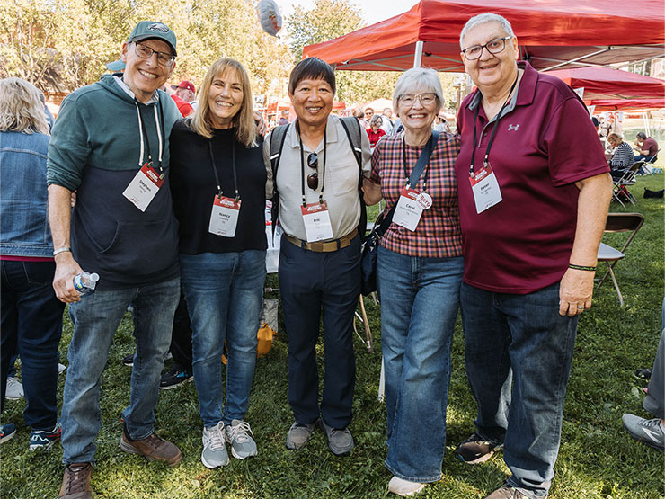 A group of Muhlenberg alumni stands, arms over shoulders, and smile on the campus of Muhlenberg College.