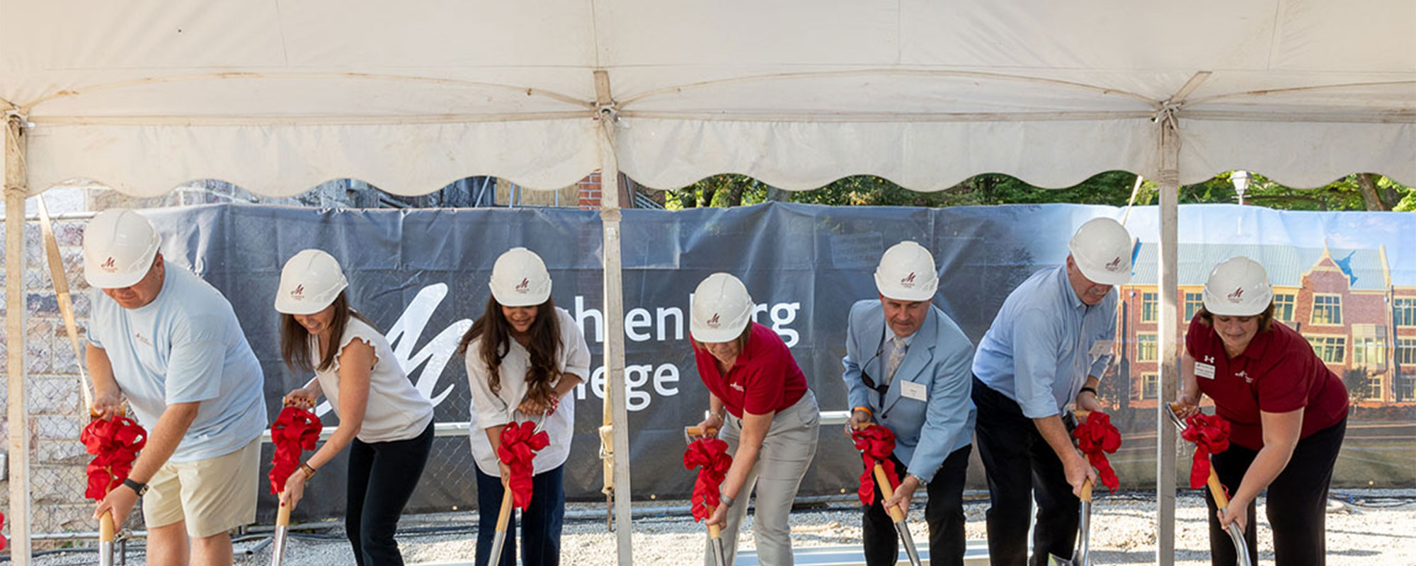 A group of people in white hard hats dig into the earth with ceremonial shovels.