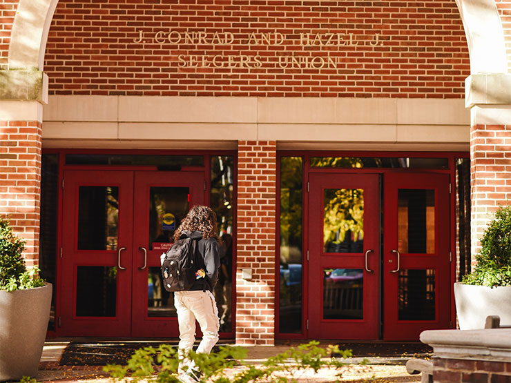 A college student walks into a red brick building that reads 