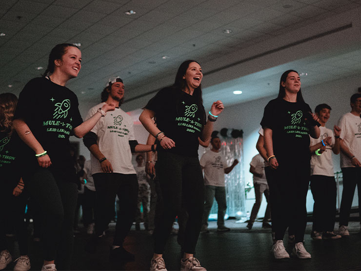 A group of college students with Mule-A-Thon t-shirts dance in unison.