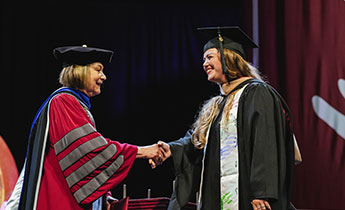 A graduate student dressed in commencement regalia shakes hands with Muhlenberg College President Kathleen Harring after receiving a degree.
