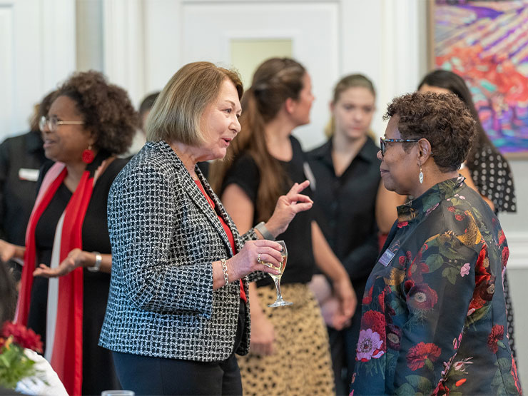 A room full of adults of various racial backgrounds converse with one another, while sipping drinks.