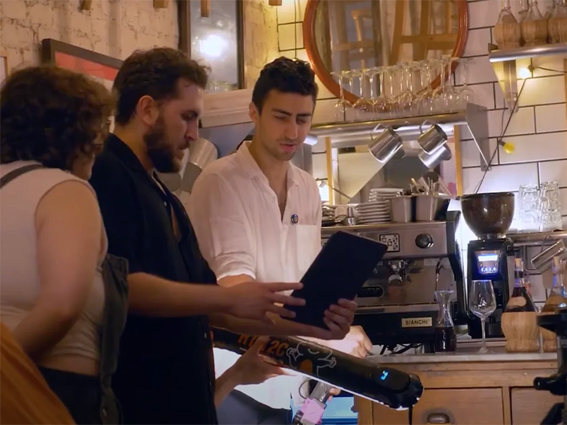 Three young people gather around an iPad in a restaurant during a video shoot