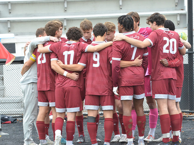 The Muhlenberg men's soccer team gathers in a circle, arms around one another's shoulders.