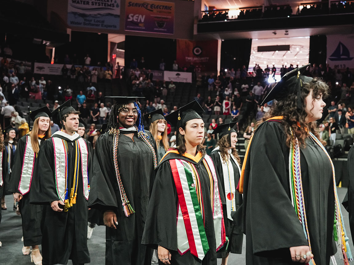 A group of college students in commencement regalia file into the ceremony