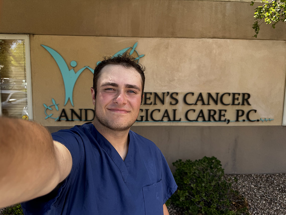 A college student in blue scrubs takes a selfie