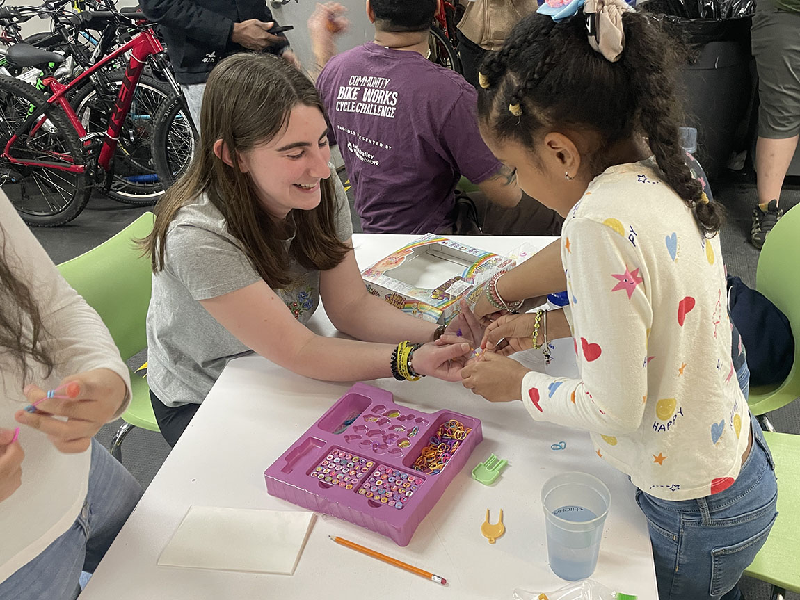 A college student works with a young girl at a bike shop
