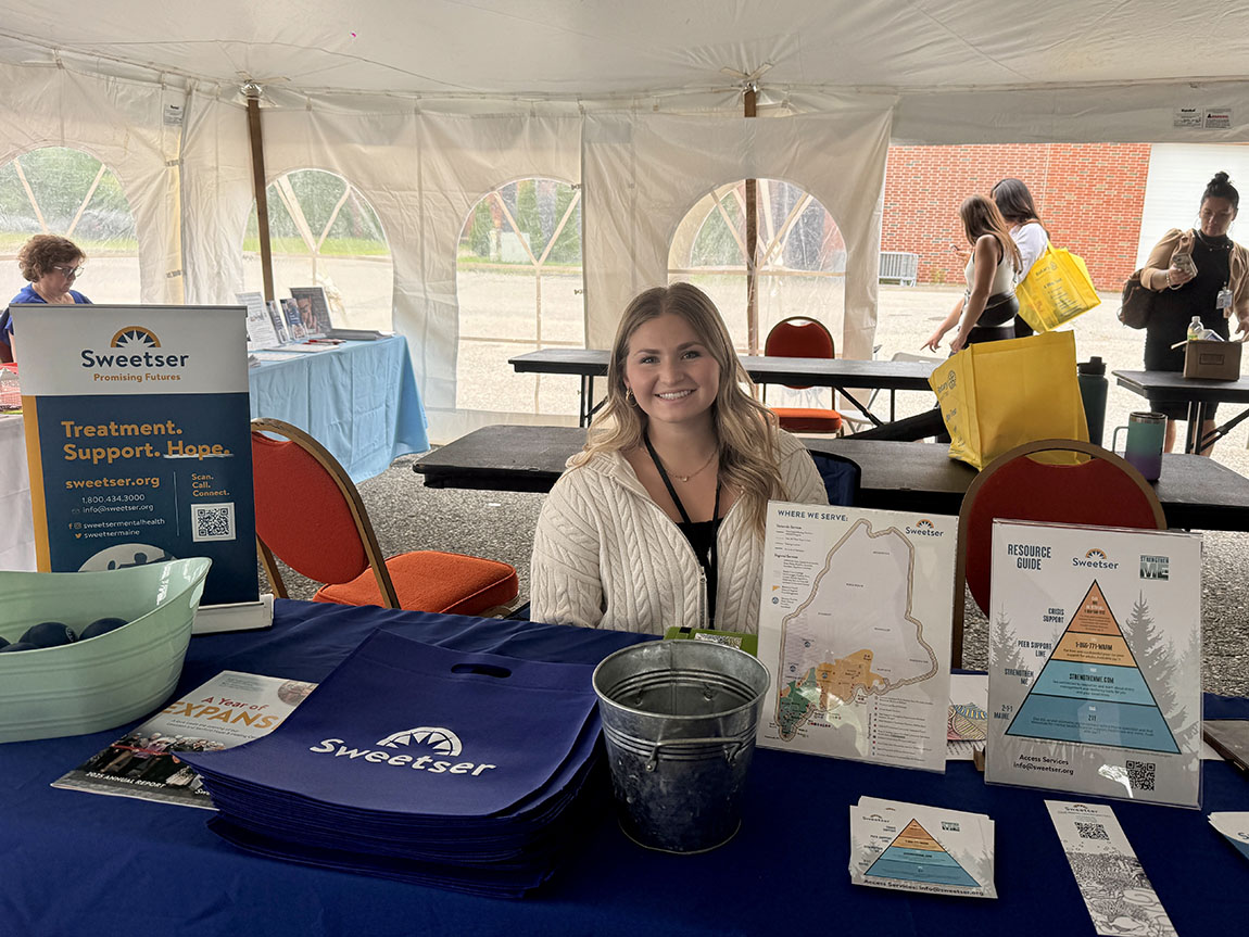 A college student sits at a table with brochures and other information displayed