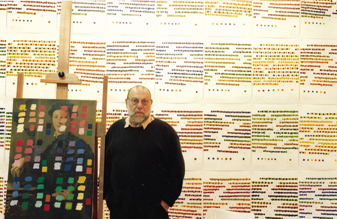 An older artist stands in a room with color swatches and a painting