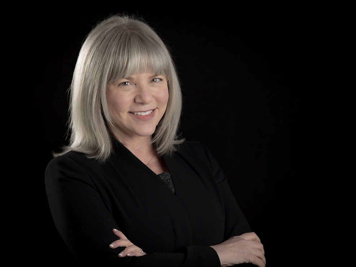 A headshot of a woman in a black shirt on a black background