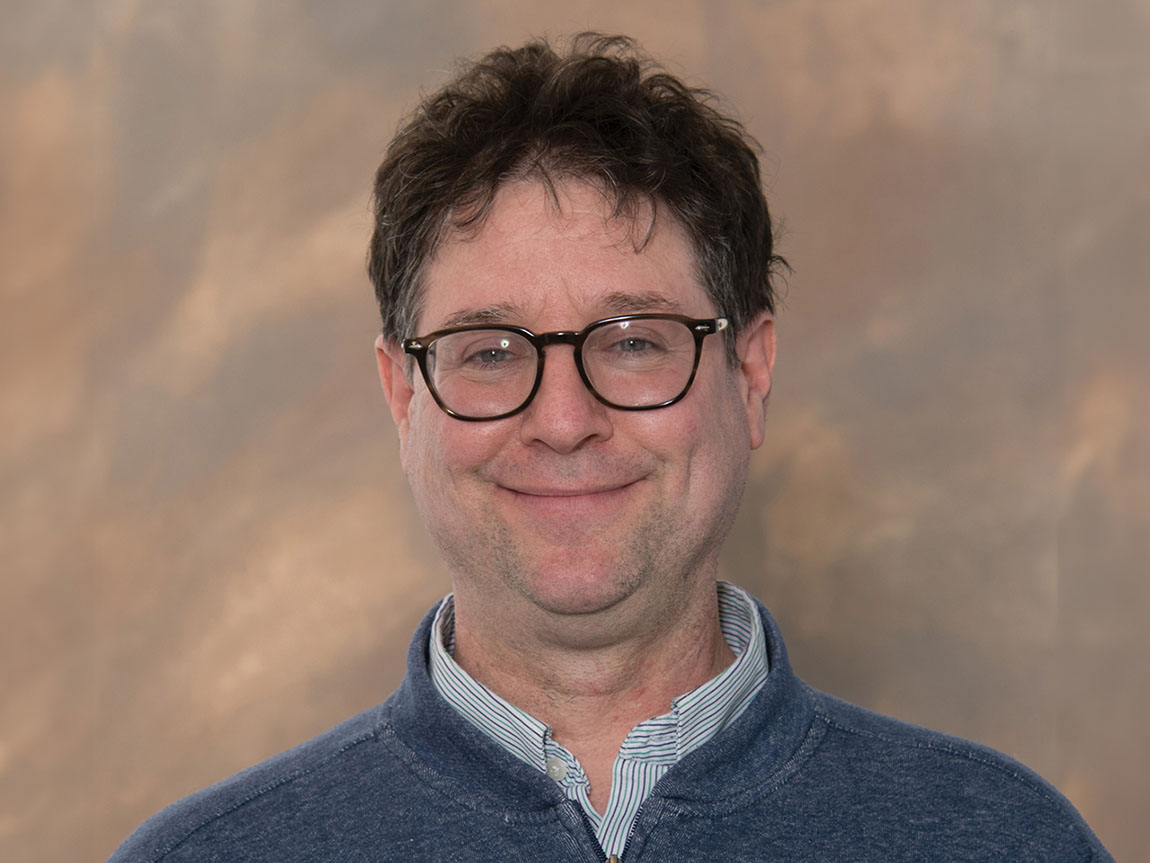 A college professor with short hair and glasses poses for a headshot