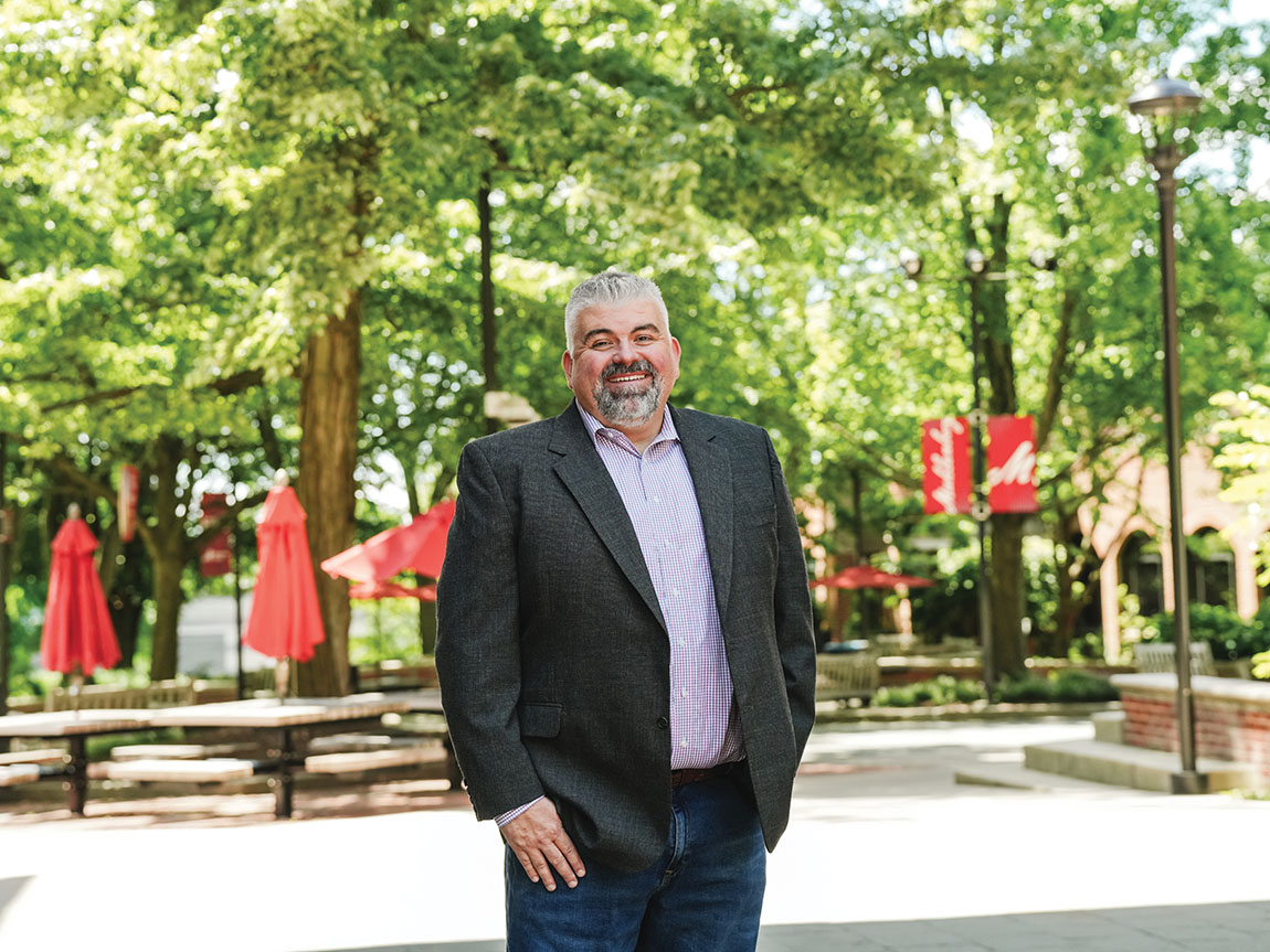 A man in a suit stands for a portrait outside on a college campus