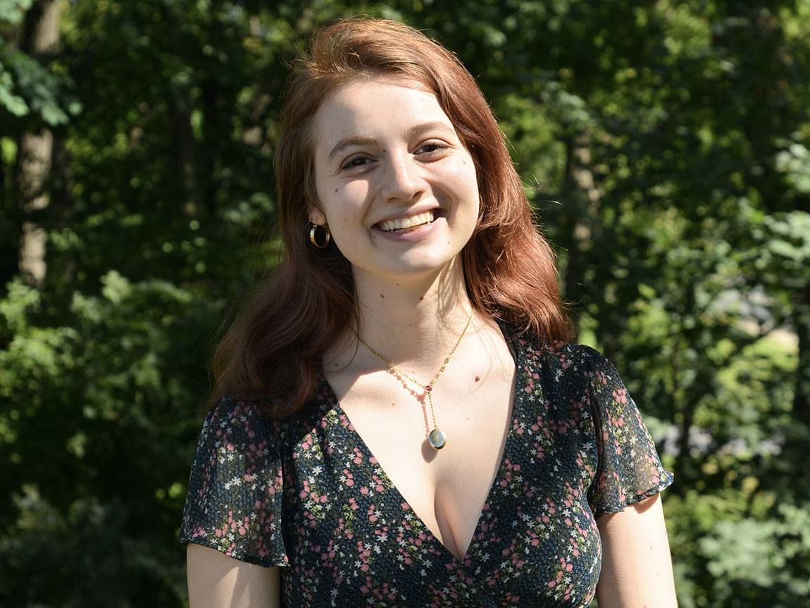 A headshot of a college student with long hair outside