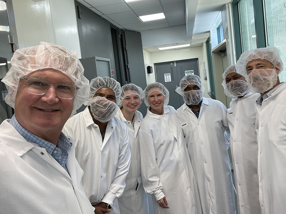 A group of people in lab coats and hair nets smile inside a laboratory