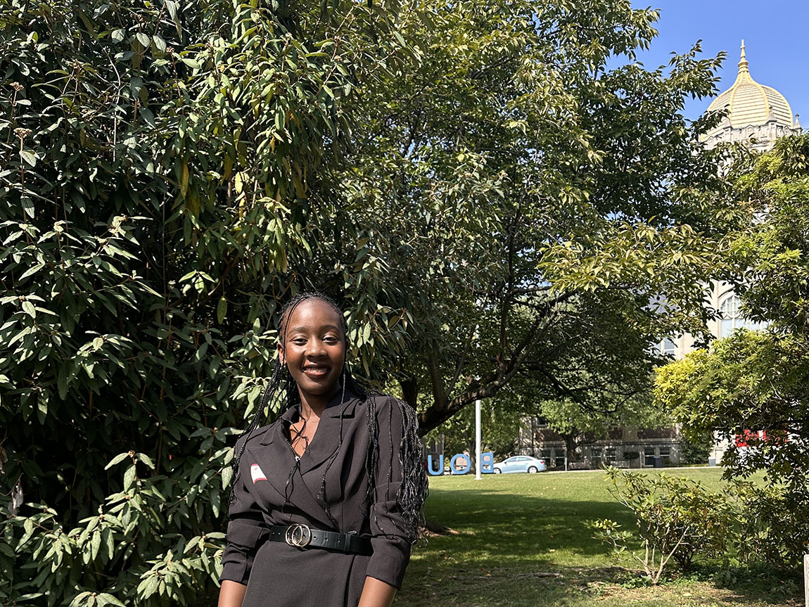 A college student in a black dress poses for a portrait outside