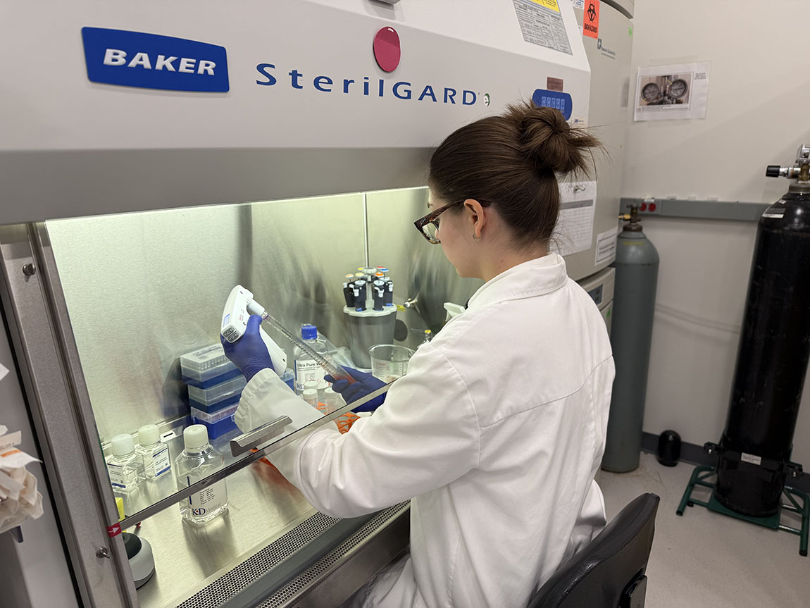 A college student in a lab coat works with lab equipment with her back to the camera
