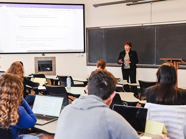 A college instructor stands and speaks to a classroom full of students.